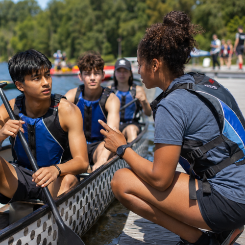 Youth in a canoe listen to their coach who is on the dock