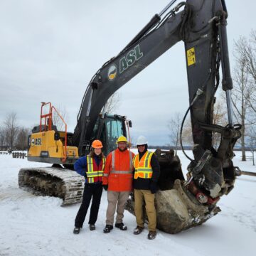 Photo of 3 people standing next to a large excavator
